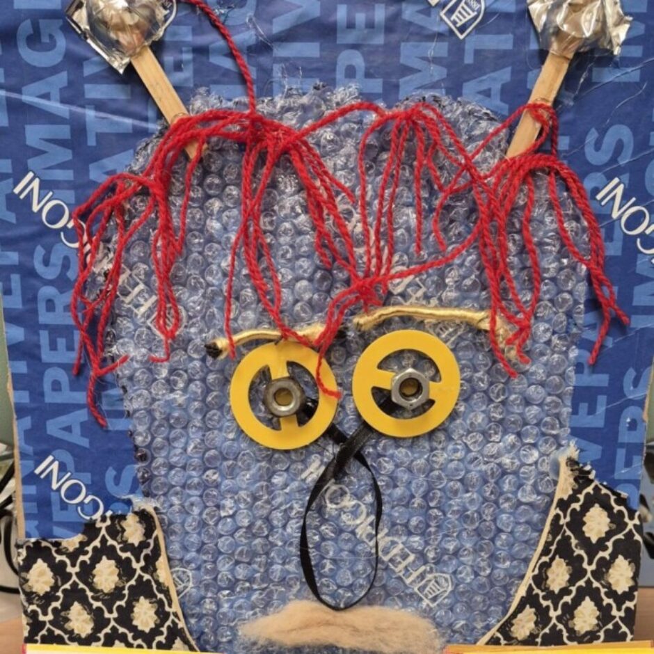 Kolāža ar cilvēka seju, veidota no auduma, pogām, papīru un dabas elementiem.