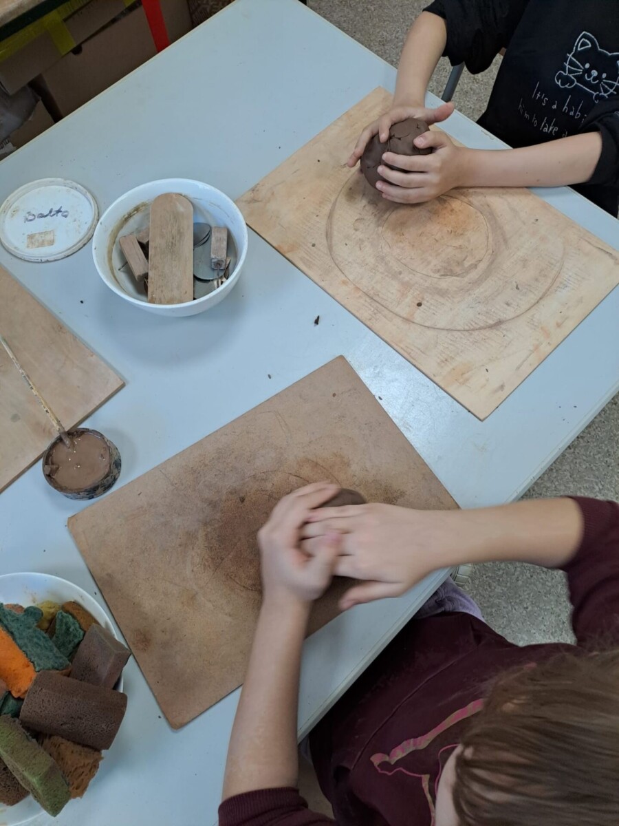 Divi bērni sēž pie galda un strādā ar mālu.