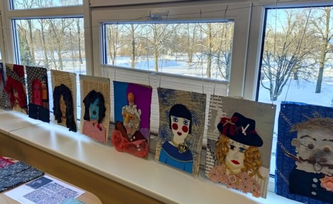 Vairāki dažādu materiālu kolāžu darbi, galvenokārt stilizēti portreti, ir izkārti rindā uz palodzes. Aiz tiem pa logu redzama sniegota ziemas ainava ar kokiem.